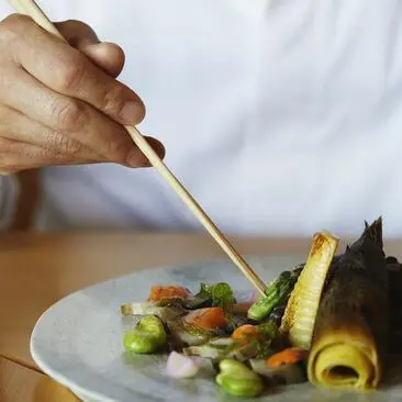 Hand plating a colourful vegetable dish at Amanemu, with a garnish being added to the plate.