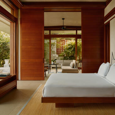 Spacious bedroom at Amanera with warm wooden walls, large bed, and open doors leading to garden views.