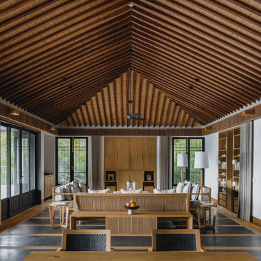 Amanoi residence living pavilion with timber ceiling, wooden furnishings and floor-to-ceiling windows overlooking Vietnamese landscape.