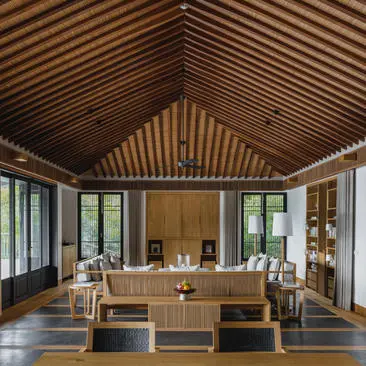 Amanoi residence living pavilion with timber ceiling, wooden furnishings and floor-to-ceiling windows overlooking Vietnamese landscape.