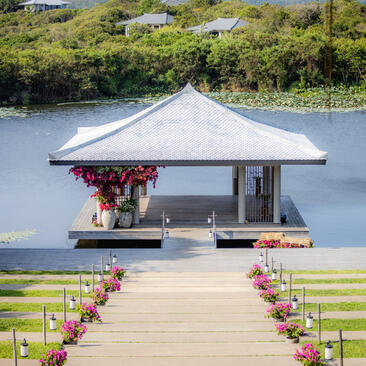 White wedding pavilion on wooden jetty at Amanoi, Vietnam, with flower-lined aisle overlooking tranquil water and forested mountains.