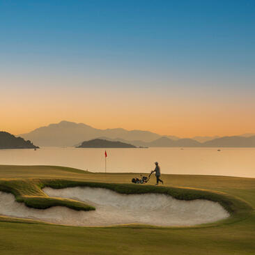 Golf course at Amanoi with sand bunker, fairway and coastal mountains at dawn.
