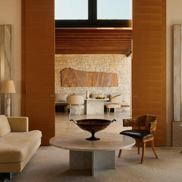 Pavilion accommodation interior at Amanzoe resort with cream seating, stone fireplace and warm wood panelling.
