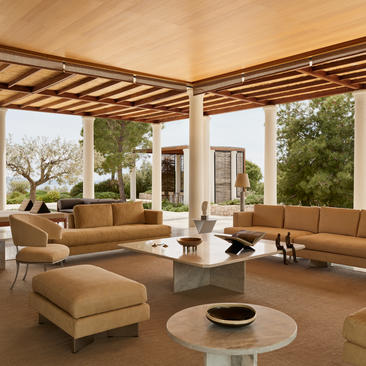 Villa lounge dengan sofa beige, pemandangan taman, dan langit-langit kayu di Amanzoe resort.
