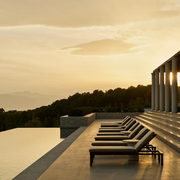 Villa terrace with loungers overlooking still waters at Amanzoe resort, Greece, at dusk.