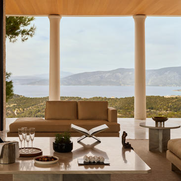 安缦卓熠度假村的别墅起居室，宽敞的落地窗框出海景和远山景观，米色沙发和大理石茶几营造温和舒适的氛围。
