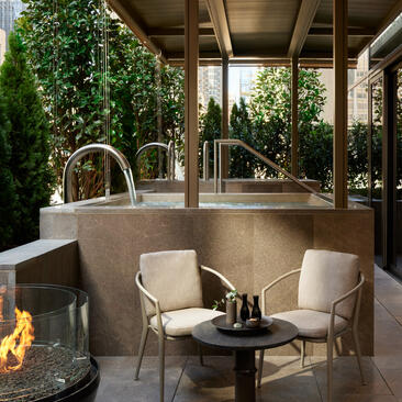 Terrazza dell'Aman New York con due poltrone crema intorno a un tavolino nero, pareti verdi e camino.