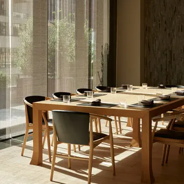 Salle à manger privée à Aman New York, avec table en bois et chaises, baignée de lumière naturelle.