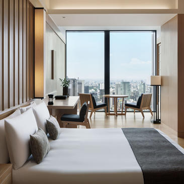 Principal bedroom with city views at Aman Tokyo, featuring bed and lounge seating by floor-to-ceiling windows.