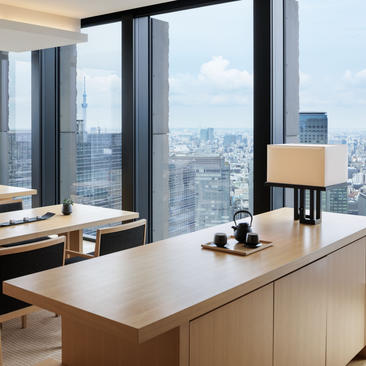 Dining suite at Aman Tokyo with floor-to-ceiling windows overlooking the city skyline, wooden cabinetry, and minimalist furnishings.
