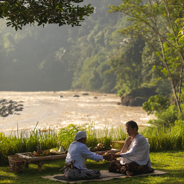 Two guests seated on grass overlooking a river at Amanjiwo, Central Java, during a wellness retreat.