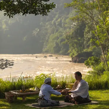 Two guests seated on grass overlooking a river at Amanjiwo, Central Java, during a wellness retreat.