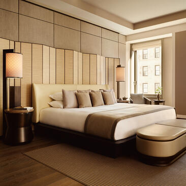 Principal bedroom with cream upholstered headboard and modern furnishings at Aman New York.