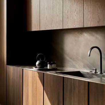 Modern kitchen at Aman New York with wood cabinetry, black countertop, and stainless steel sink.