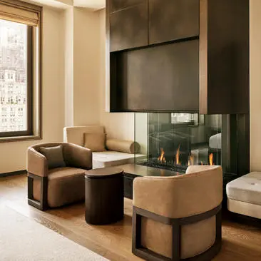 Living room in a three-bedroom residence at Aman New York, with caramel leather chairs, a flat-screen television, and city views.