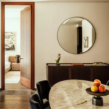 Living area of a one-bedroom home at Aman New York, featuring a round mirror, dark furniture, and view through to an adjoining room.