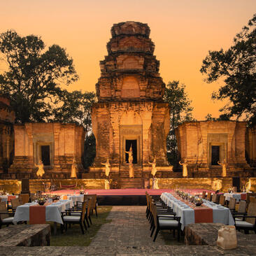 Candlelit dining set up in a courtyard at Amansara, with a temple illuminated at dusk in Cambodia.