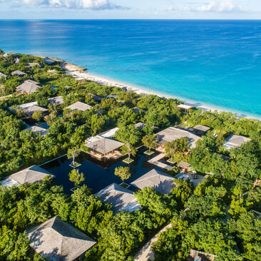 Aerial view of Amanyara villa nestled amongst tropical vegetation along turquoise coastline.