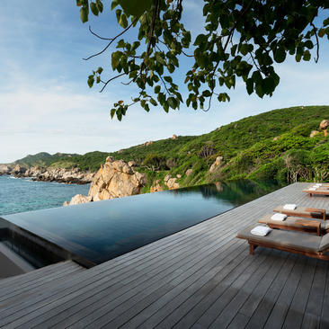 Wooden terrace with sun loungers overlooking a tranquil cove at Amanoi, framed by lush hillside and clear turquoise waters.