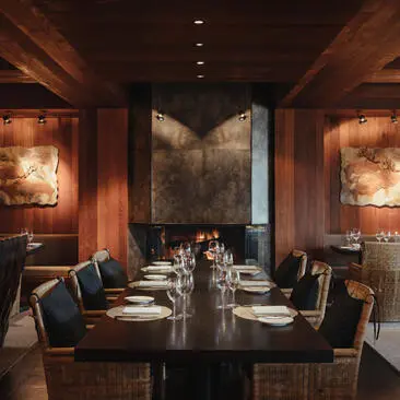 Intimate dining room at Amangani with timber-lined walls, long table set for service, and floor-to-ceiling windows overlooking mountain landscape.