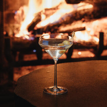 Cocktail glass on table with fireplace glowing in background at Amangani.