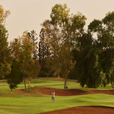 Terrain de golf du resort Amanjena au Maroc, avec joueurs sur le parcours verdoyant.