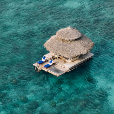 Aerial view of the floating Kawayan Bar at Amanpulo, Philippines, with thatched roof structure on turquoise water.