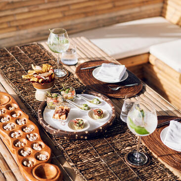 Floating Kawayan bar picnic setup at Amanpulo, with oysters, glasses, and place settings arranged on a woven surface.