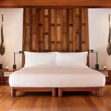 Principal bedroom at Amanpuri with wooden headboard and white bedding against white walls.
