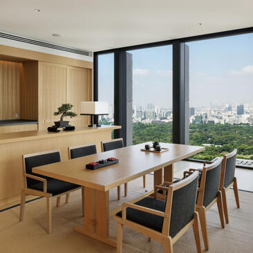 Aman Suite dining area at Aman Tokyo with wooden table, city views through floor-to-ceiling windows, and open-plan kitchen.
