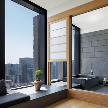 Aman Tokyo suite bathroom with floor-to-ceiling window overlooking the city skyline and wooden accents.