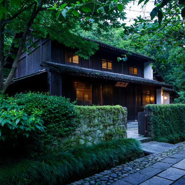 Modern black pavilion at Amanfayun nestled amongst lush green foliage at dusk, warm interior lights glowing.
