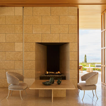 Fireplace with two chairs in a warm stone room at Amanzoe, overlooking the Greek coastline.