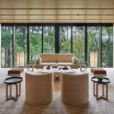 アマン京都のリゾートにある、大きな窓から庭園を望む円形のラウンジエリア。タン色のソファと木製の小テーブルが配置されている。