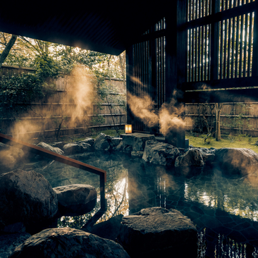 Steam rises from an indoor onsen pool at Aman Kyoto, with wooden architecture and natural light filtering through slatted screens.