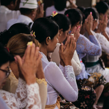 Amandari resort guests participating in a Piodalan ceremony in Ubud, Bali, with hands clasped in prayer.