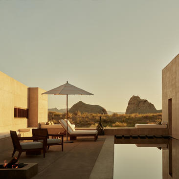 Amangiri suite with lounge seating, umbrella and reflecting pool overlooking desert landscape at dusk.