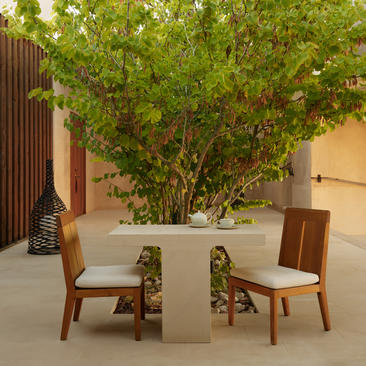 Girijaala Suite seating area at Amangiri, with two wooden chairs facing each other beside a large shaded tree.