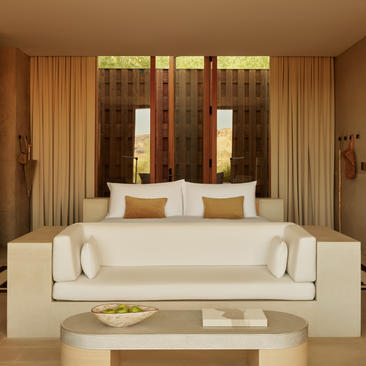 Mesa Suite living area at Amangiri resort, featuring a cream sofa with golden curtains and dark wooden doors.