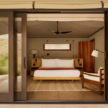 Camp Sarika accommodation pavilion bedroom at Amangiri, featuring a bed with warm wooden furnishings and open glass doors.