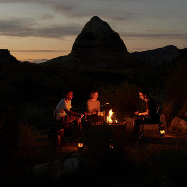 Guests gather around a campfire at dusk beneath a dramatic rock formation at Amangiri's s'mores pavilion.