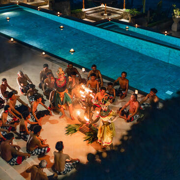Balinese dancers perform at Amankila resort, viewed from above with an illuminated poolside gathering below.