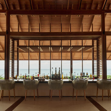 Beach Club bar at Amanyara resort with wooden ceiling and ocean views through large windows.