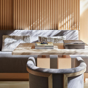 アマン京都のリゾートに位置する、木製スクリーンを背景にした寝室。ベッドの前には、折り畳まれたリネンと装飾品が置かれたモダンなテーブルがある。