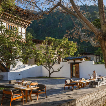 Outdoor dining terrace at Aman Punakha with wooden furniture and mountain views beyond.