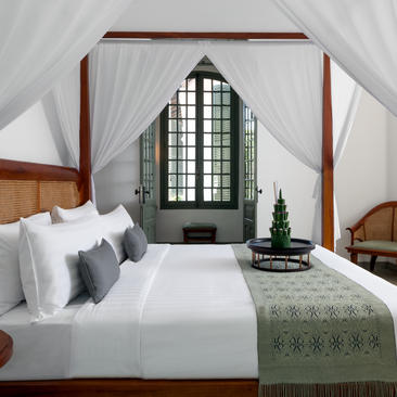 Principal bedroom with four-poster bed, white linens, and arched window at Amantaka.