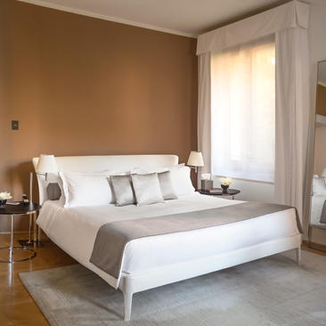 Palazzo principal bedroom with white bed and warm ochre walls at Aman Venice hotel.