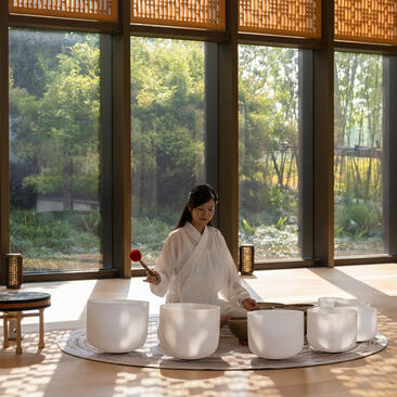 Woman arranging white ceramic sound bowls at Amanyangyun, sunlit room with forest views.