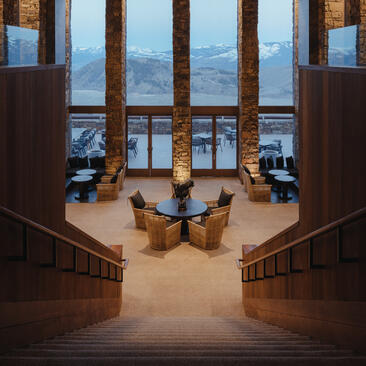Symmetrical view down a wooden staircase towards the lobby lounge at Amangani, with floor-to-ceiling windows overlooking mountains beyond.