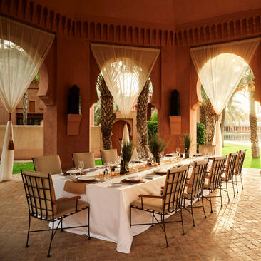 Ochre-walled gazebo at Amanjena with arched openings, dining table, and chairs bathed in natural light.